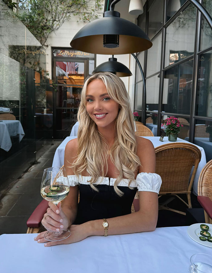 Woman with long blonde hair smiling at a restaurant, holding a glass of wine, relating to woman who slept with 583 men.
