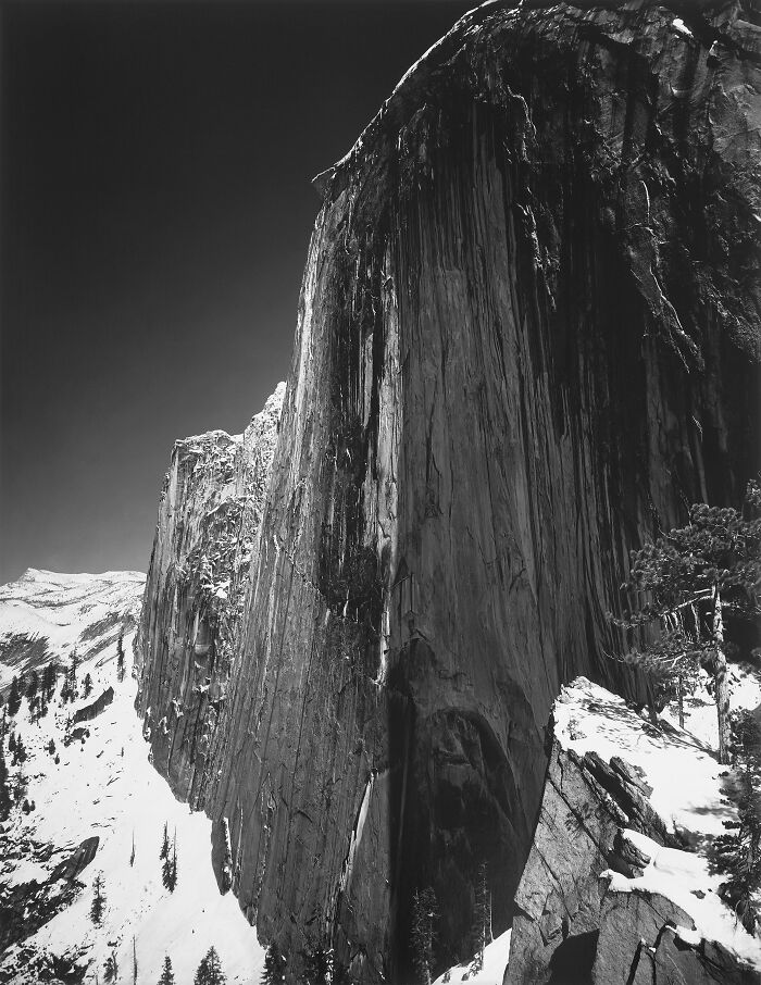 Black and white dramatic cliff face with snow-covered mountains, representing triumph and tragedy in 20th century images.