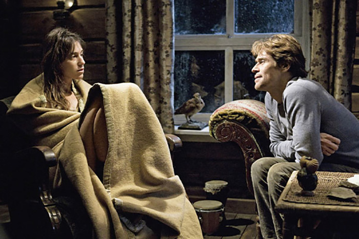 Two movie stars wrapped in blankets filming intimate love-making scenes in a dimly lit rustic room.