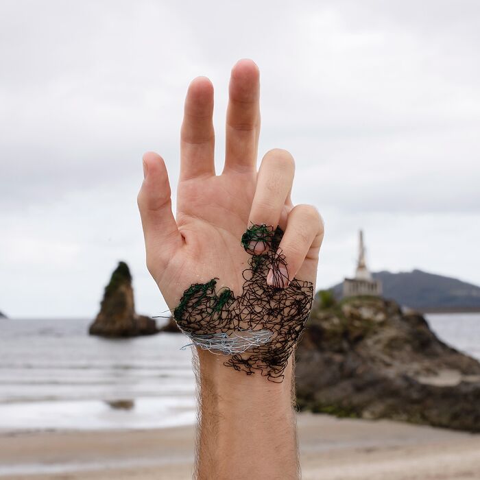Hand with landscape stitched onto skin using black, green, and white threads, blending art with nature in a stunning way.