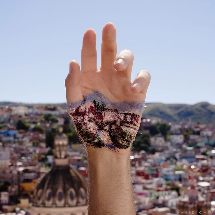 Hand with a detailed landscape stitched onto the skin, showcasing intricate embroidery art and creative body stitching technique.