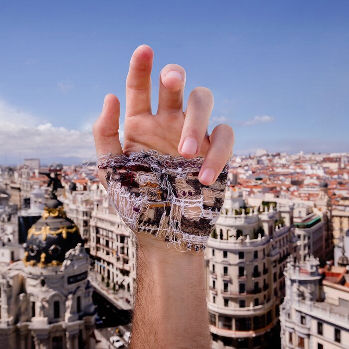 Hand with stitched landscape art on skin, held against a cityscape background, showcasing unique stitched landscapes.