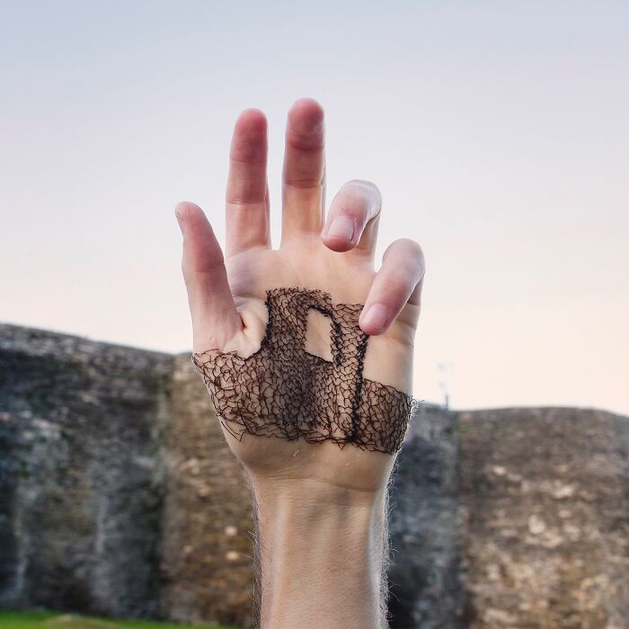 Hand with detailed landscape stitching art on skin, showcasing the artist's unique skill in landscape skin stitching.