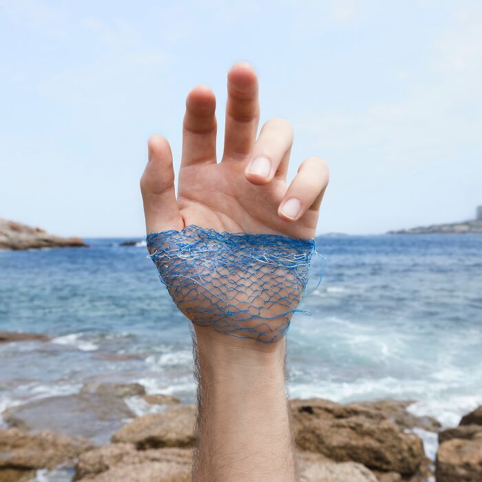 Hand with blue thread stitched on skin, set against a rocky seascape, showcasing unique landscape skin art.