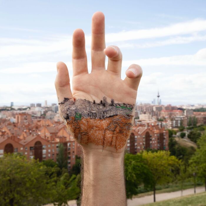 Hand with a stitched landscape art piece on the skin, blending cityscape and nature elements in detailed embroidery.