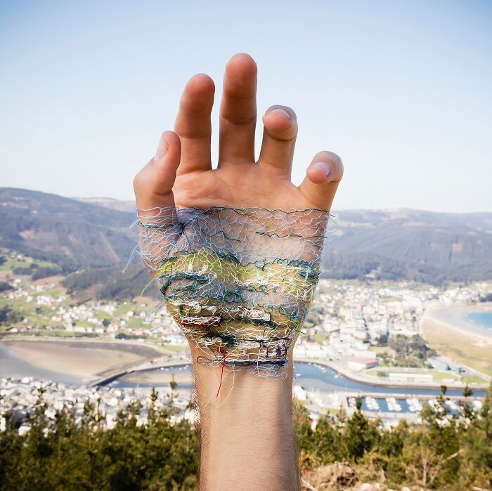 Hand with detailed landscape stitched onto skin, blending embroidery art with natural scenery in a creative outdoor setting.