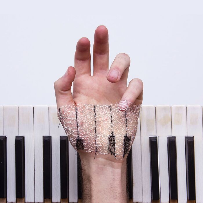 Hand with intricate stitching resembling a landscape art piece over the skin, placed above piano keys.