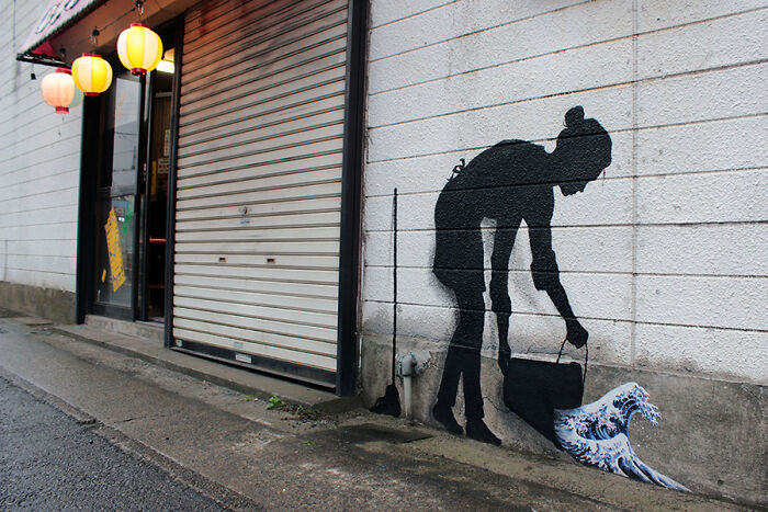 Street art photo of a black silhouette woman pouring water that turns into a wave on a white brick wall.