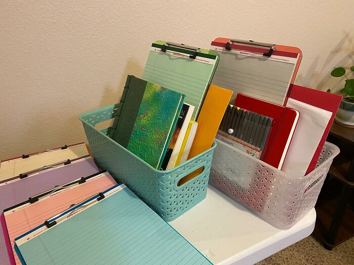 Two baskets filled with back to school supplies including clipboards, notebooks, and pens on a white table.