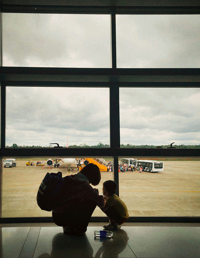 Passenger and child waiting at airport gate with airplane and crowd outside, reflecting on worst experience with bored child on flight.