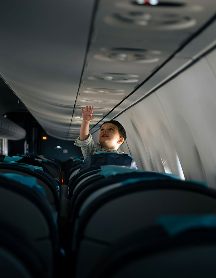 Child on flight reaching overhead compartment, highlighting passenger experience with bored child sparking debate on plane journey.