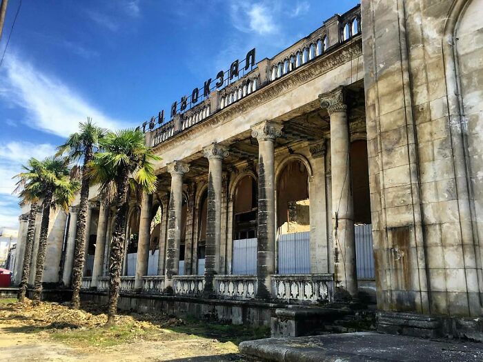 Abandoned place with weathered columns and palm trees under a bright blue sky, showing decay and neglect.