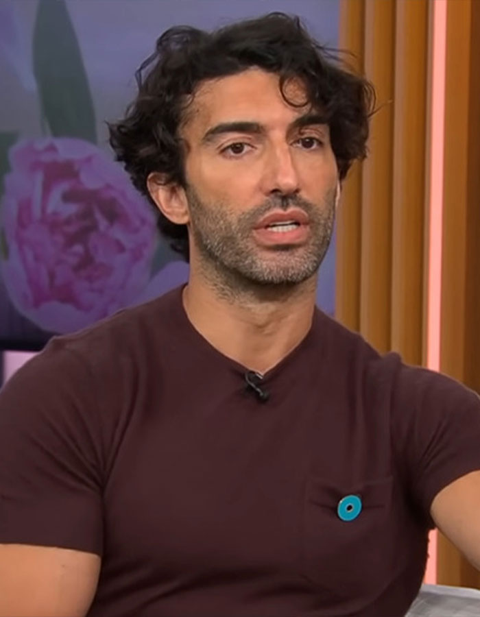 Man with curly hair and beard wearing a brown shirt, speaking during an interview about Blake Lively rom-com role.