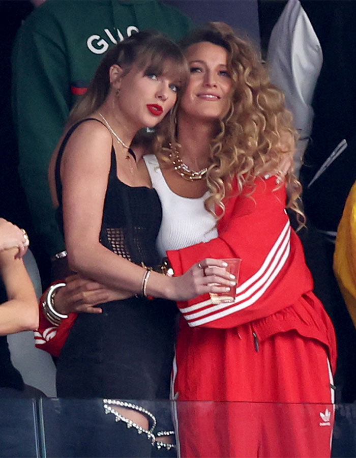 Blake Lively in red outfit hugging a woman in black dress, related to leading role in new rom-com controversy.