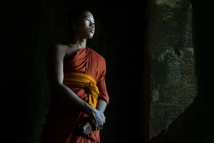 Young monk in traditional robe illuminated by natural light, showcasing cultural beauty captured by photographer traveling to 50+ countries.