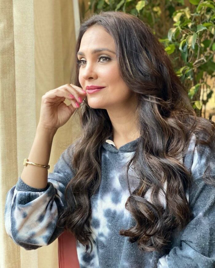 Miss Universe winner with long wavy hair and natural makeup, sitting thoughtfully by a window in casual attire.