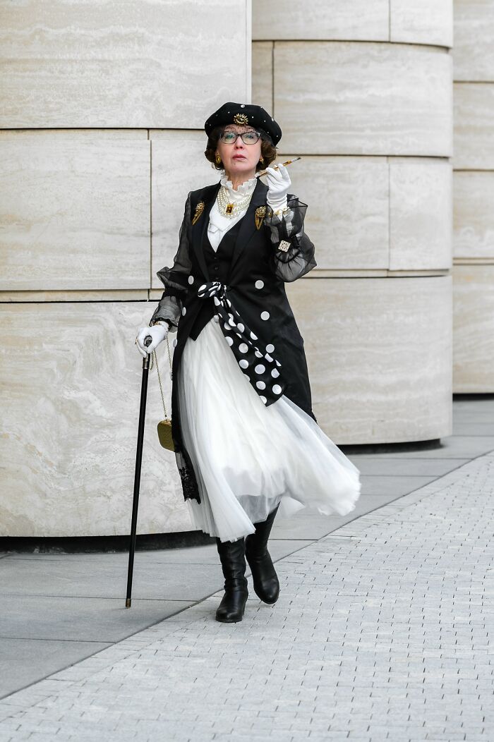 Woman in an elaborate cosplay outfit with a cane and hat walking confidently on a city street.