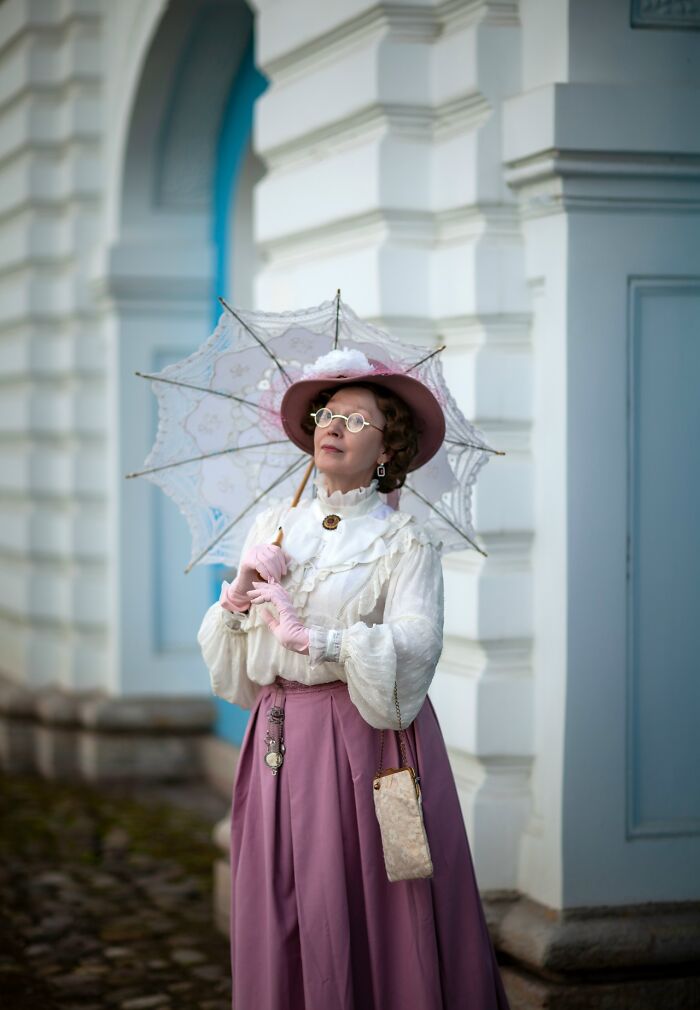 Woman in vintage costume holding a lace parasol, showcasing incredible cosplays in an outdoor historic setting.