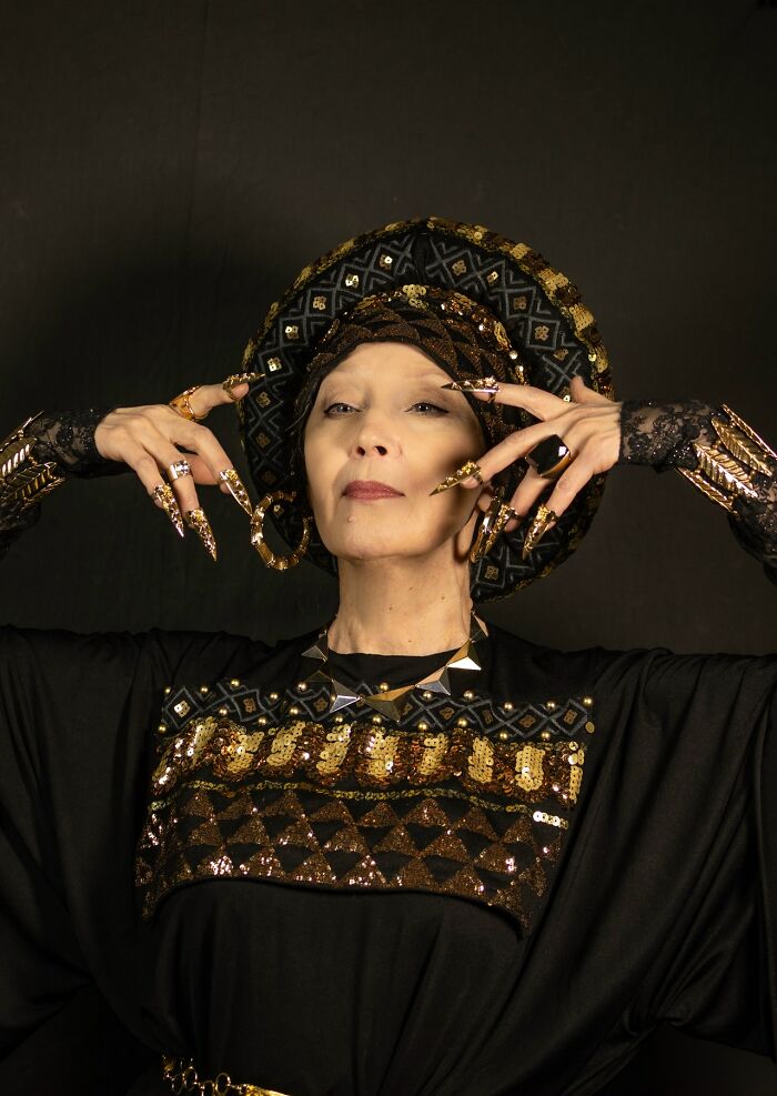 Woman in detailed black and gold cosplay with elaborate nails and headpiece, showcasing incredible cosplay craftsmanship.