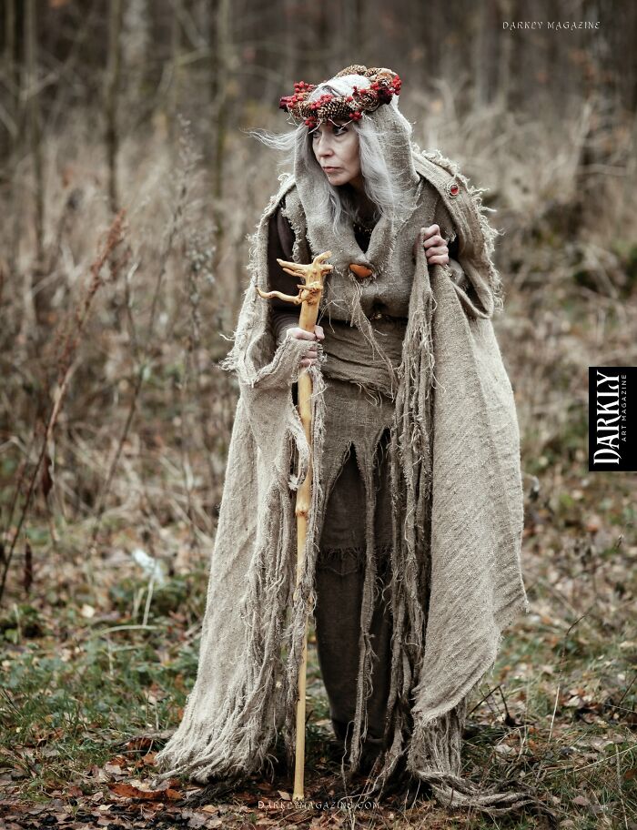 Woman in an incredible cosplay costume with a staff, wearing tattered robes and a floral headpiece in a forest setting