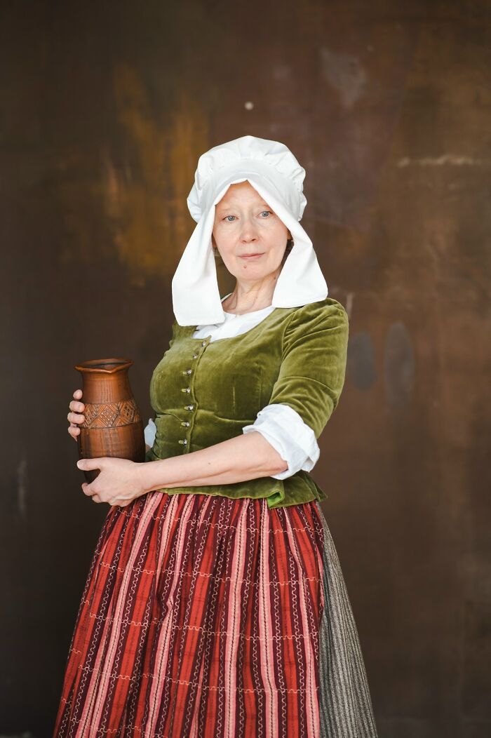 Woman in detailed historical cosplay costume holding a ceramic jug, showcasing incredible cosplays with authentic period clothing.