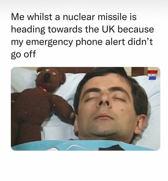 Man sleeping peacefully with teddy bear, caption about ignoring emergency alerts amid chaotic British memes humor.