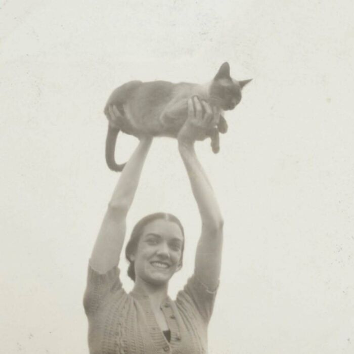 Vintage cats photo showing a smiling woman holding a cat above her head in an old-fashioned black and white style.