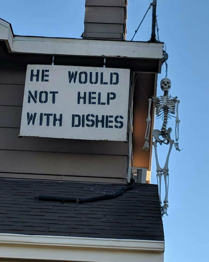 Sign reading he would not help with dishes hangs on house exterior with a skeleton figure, showcasing ingenious crafty ideas.