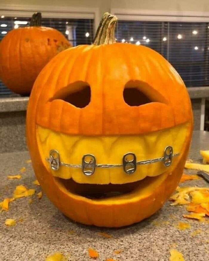 Carved pumpkin with a creative smiling face featuring braces made from soda can tabs, showcasing crafty ideas.