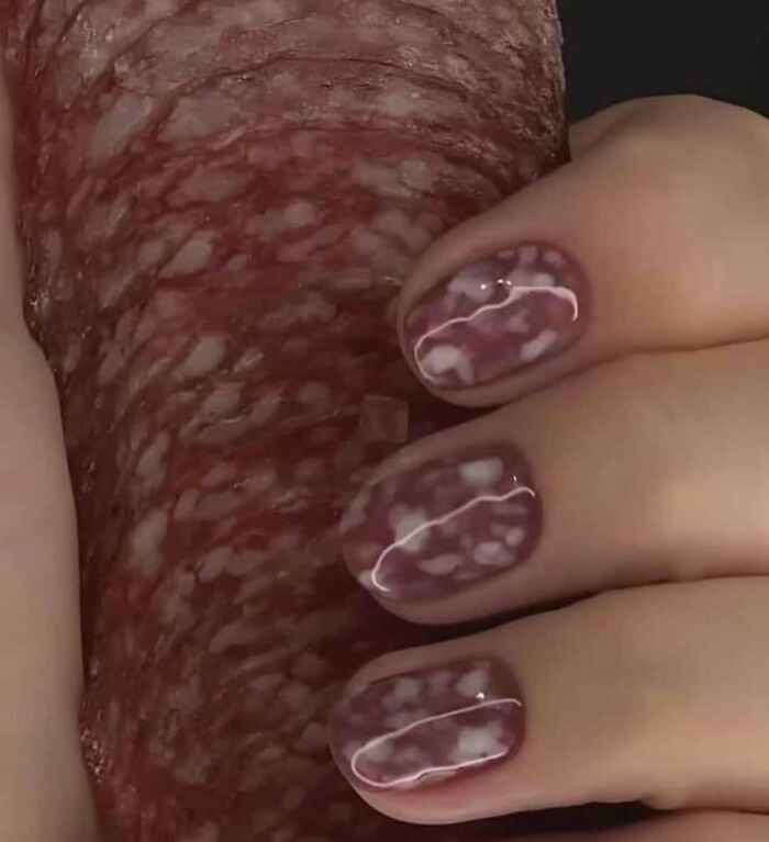 Hand with nails painted like cured meat holding a slice of salami, showcasing a cursed image from a popular IG page.