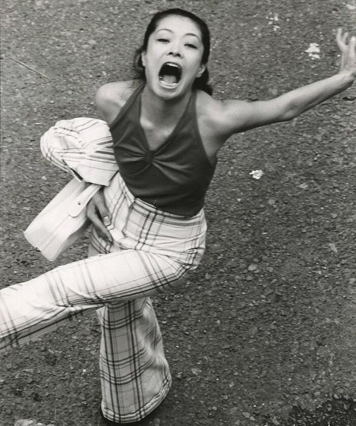 Young woman in plaid pants captured mid-motion in a candid historical photo with an emotional expression.