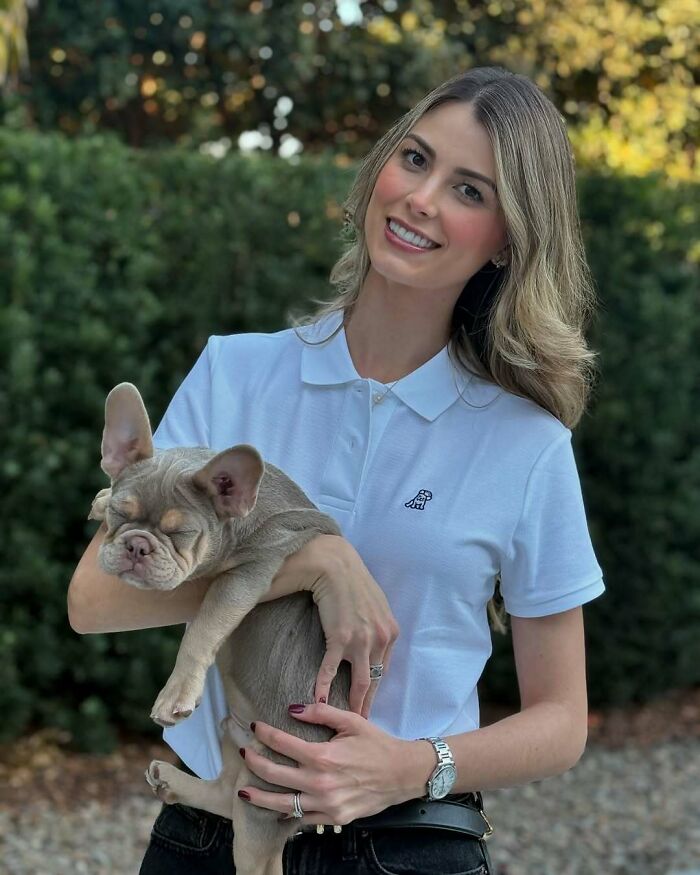 Miss Universe winner smiling outdoors holding a sleepy French Bulldog with greenery in the background.