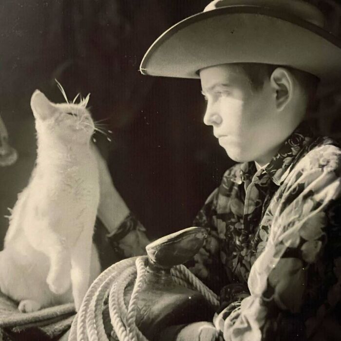 Vintage cat sitting beside a young boy dressed as a cowboy holding a rope, showcasing vintage cats charm and cuteness.