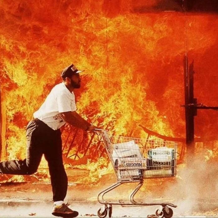 Man with shopping cart full of supplies running past large fire, illustrating moments common folk made huge mark in history.