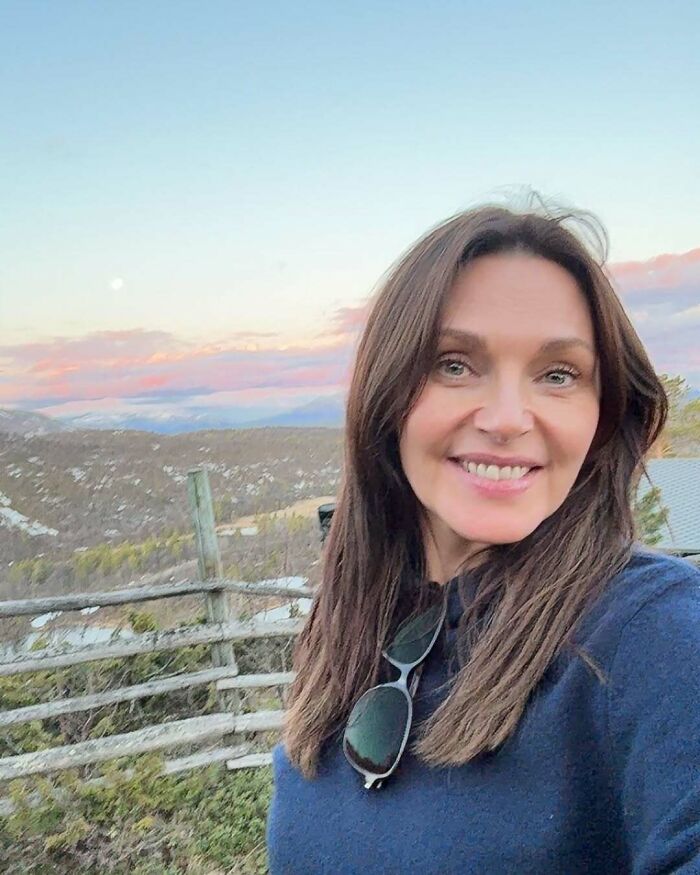 Smiling woman outdoors with mountains and a wooden fence in the background, captured in a Miss Universe winners photo.