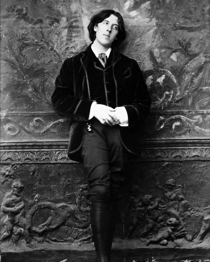 Black and white photo of a man in vintage clothing leaning against an ornate wall showing common folk's huge mark in history.