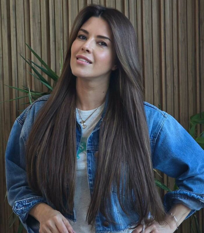 Miss Universe winner with long brown hair wearing a denim jacket posing confidently against a wooden background.