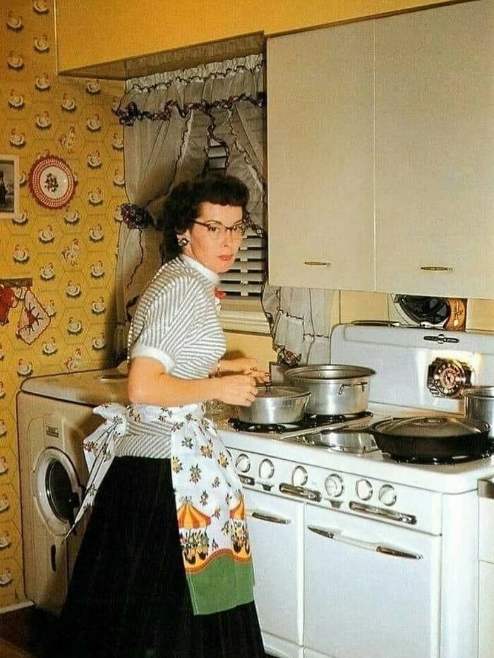 Woman in a vintage kitchen wearing apron cooking on a stove, showcasing June Cleavers vintage closet style from the past.