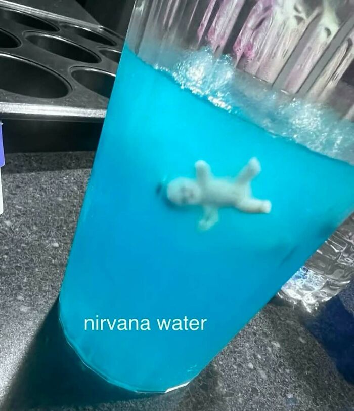 Glass filled with bright blue liquid and a small creepy human figure floating inside, a cursed image from IG page.