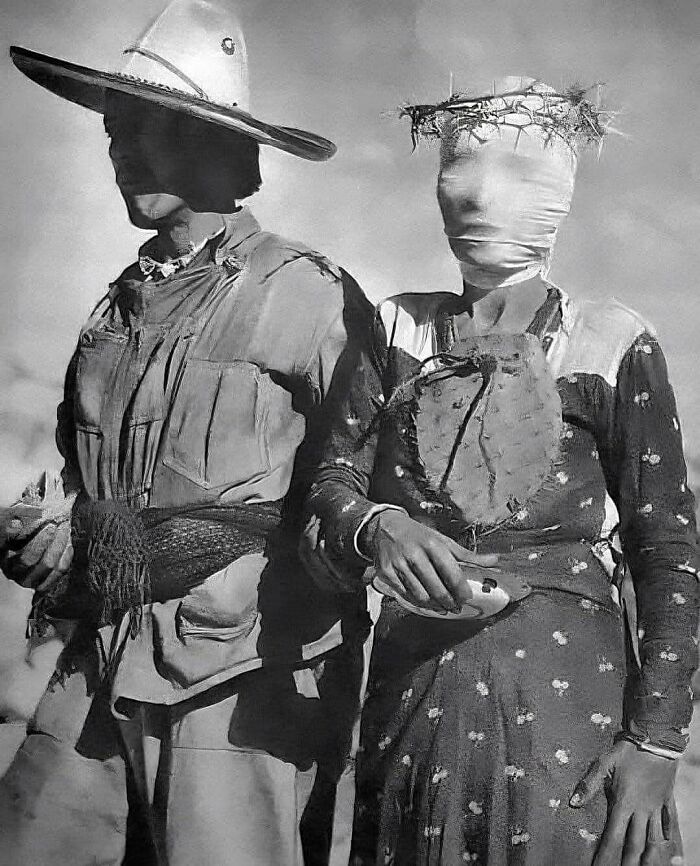 Black and white historical photo of two individuals wearing traditional clothing and unusual face coverings with a crown of thorns.