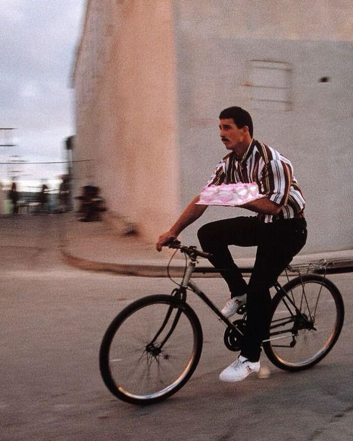 Man in striped shirt riding bike while carrying a pink package, one of the historical photos with interesting backstories.