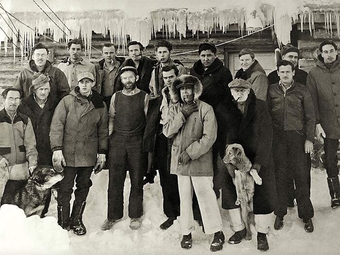 Group of men dressed in winter clothes standing in snow beneath large icicles in a historical photo with an interesting backstory