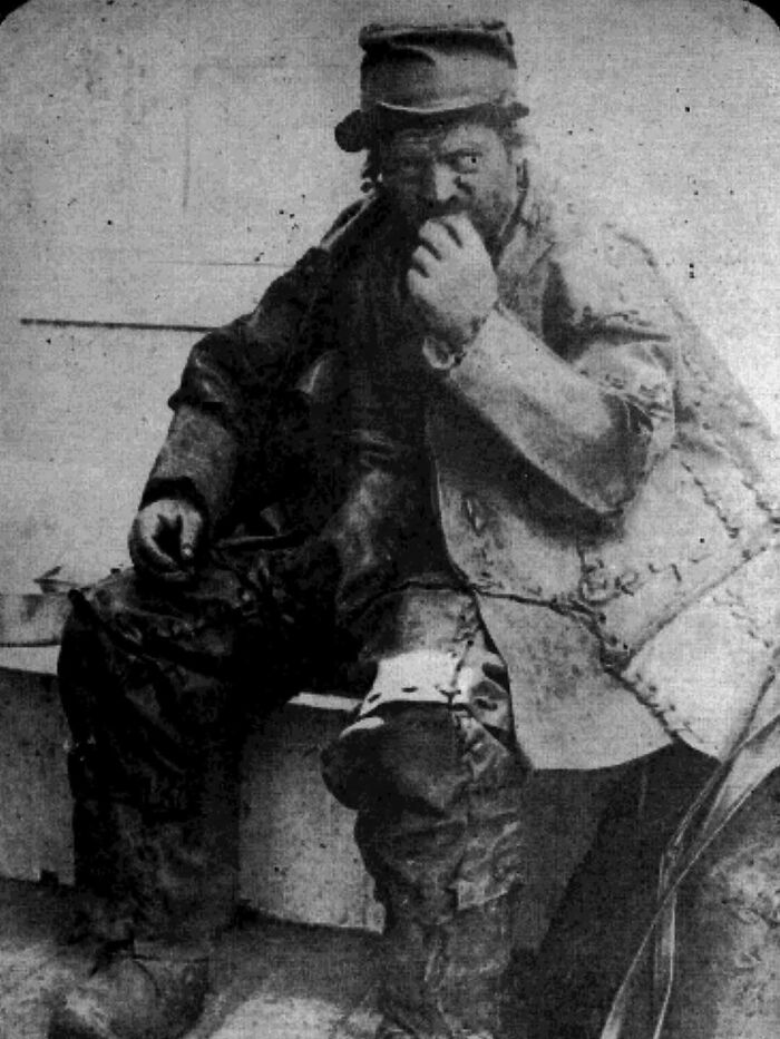 Black and white historical photo of a man in worn clothing sitting and eating, showing a heartfelt moment from the past.