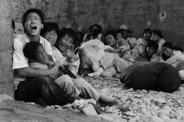 Group of common folk in distress sitting on rocky ground inside a rustic building, capturing a historic moment in society.