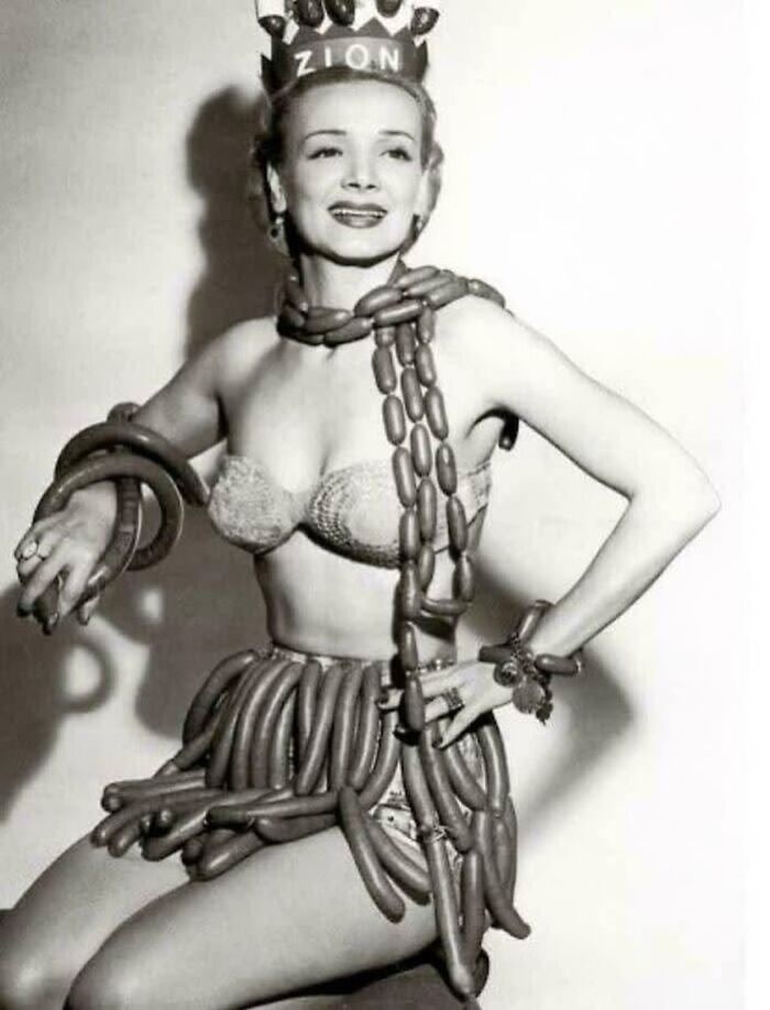 Black and white historical photo of a woman wearing a crown and costume made of sausages from vintage era.