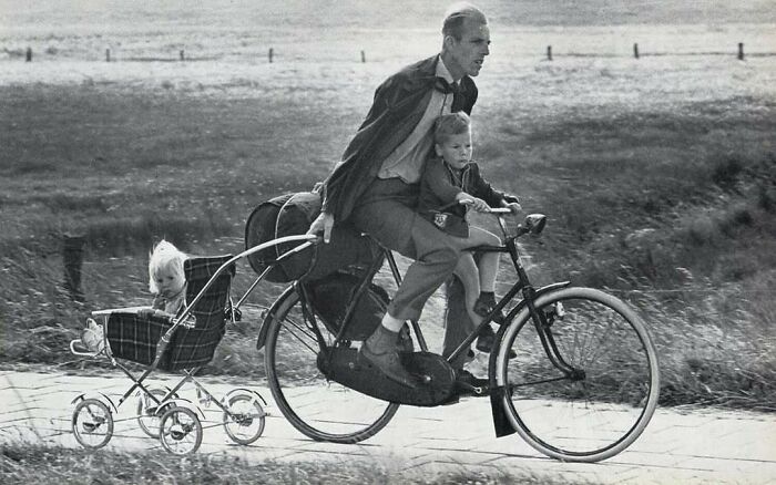 Man rides a bicycle pulling a vintage stroller with a child, capturing a moment from historical photos with interesting backstories.