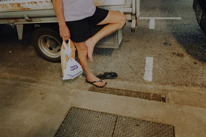Photographer captures everyday street scene with a person standing barefoot, holding a bag near a parked truck creating cinematic imagery.