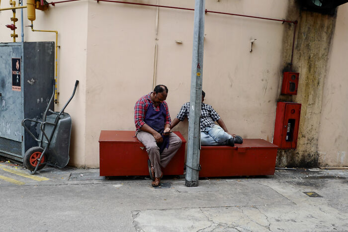 Two men resting on red benches in an urban setting, capturing ordinary moments with poetic, cinematic photography style.
