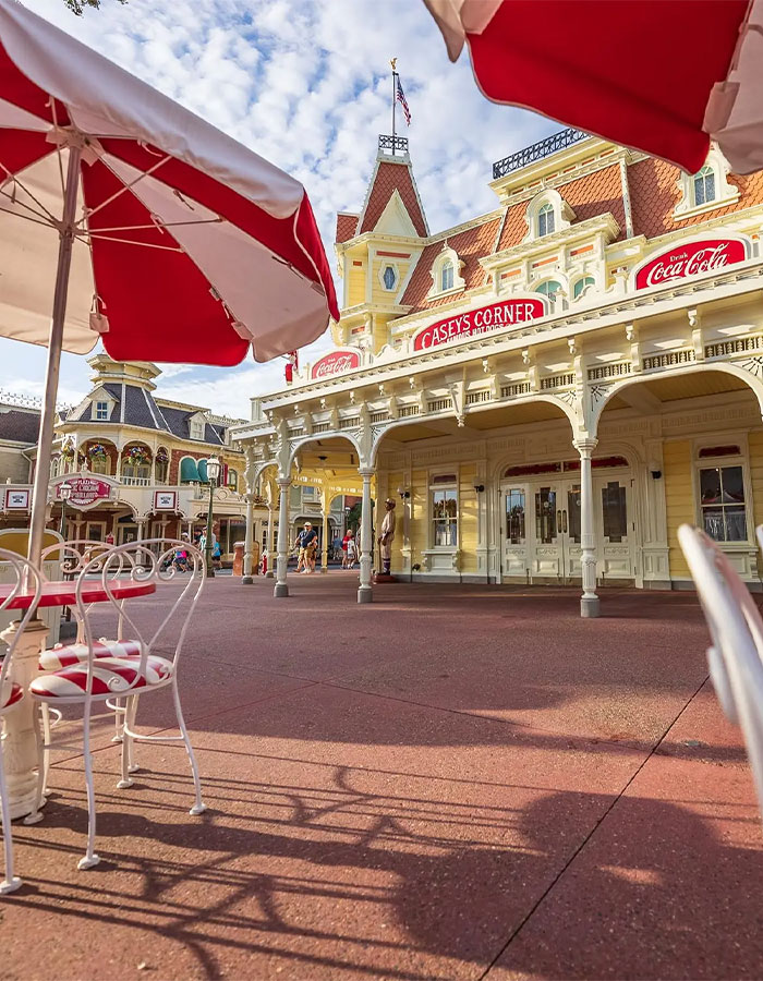 Outdoor seating with red and white umbrellas in front of Casey's Corner at Disney World during a sunny day.