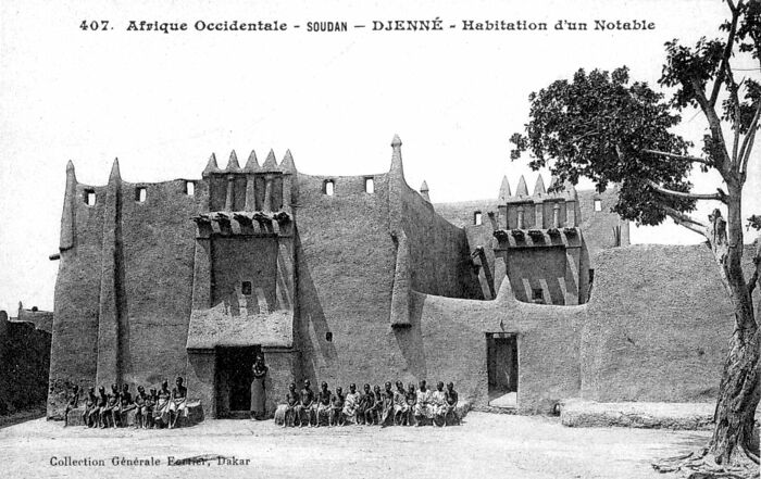 Historical photo of a traditional mud-brick building in Djenné with a group of people seated outside.